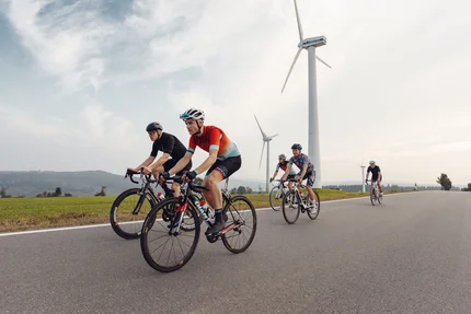 Vijf wielrenners fietsen op een weg nabij windturbines