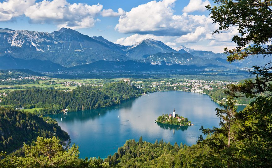 Lago con isola e chiesa, circondato da foresta e montagne sullo sfondo
