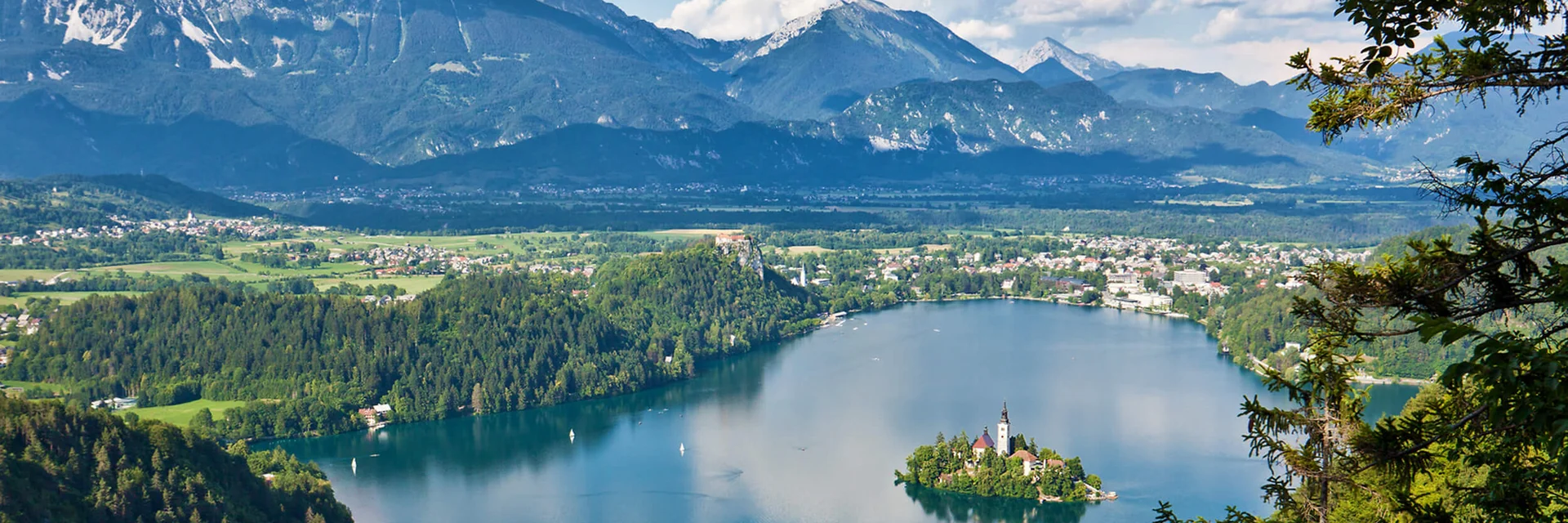 Lago con isola e chiesa, circondato da foresta e montagne sullo sfondo