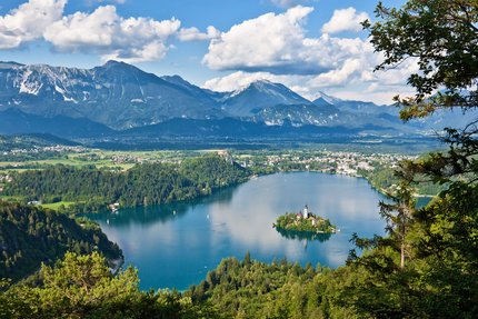 Lago con isola e chiesa, circondato da foresta e montagne sullo sfondo