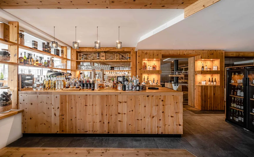 Cristallo Sport & Wellness Hotel **** © Andrea Acler Moderne Bar aus Holz mit Flaschen und Gläsern, warm beleuchtet