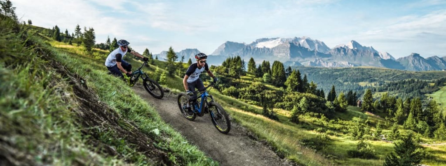 Two mountain bikers riding on a mountain trail with Alps in the background