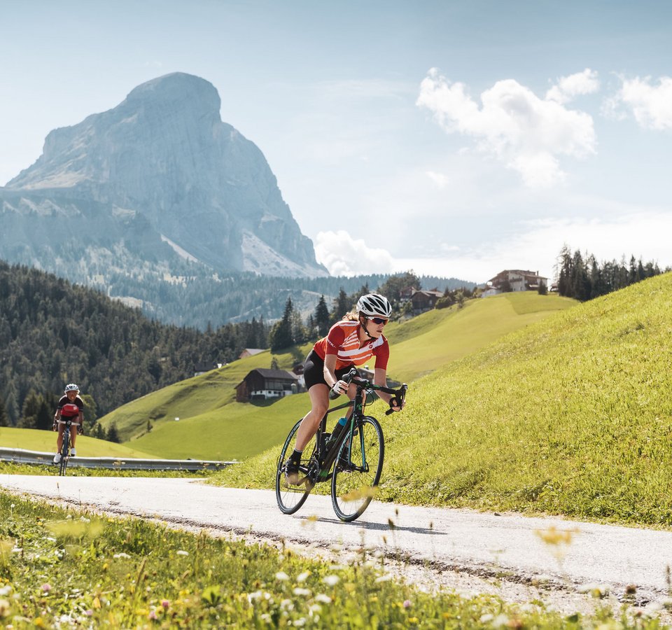 Zwei Radfahrer fahren auf Bergstraße mit Gipfel in der Sonne