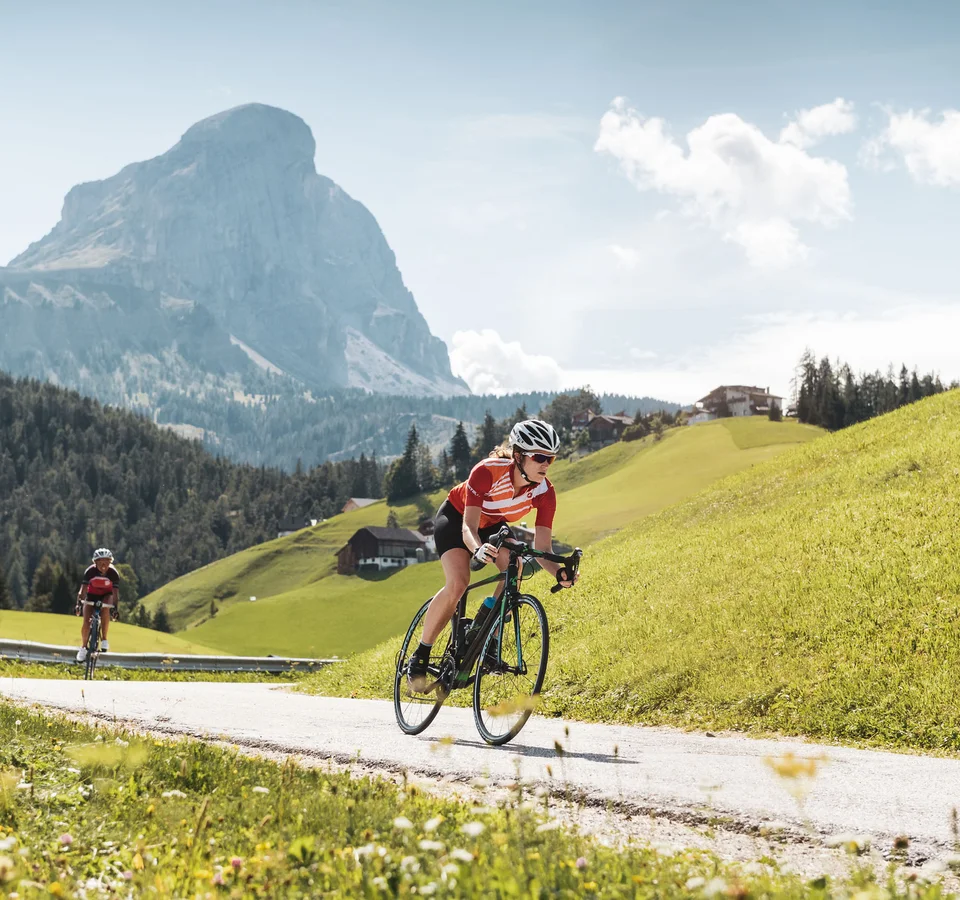 Zwei Radfahrer fahren auf Bergstraße mit Gipfel in der Sonne