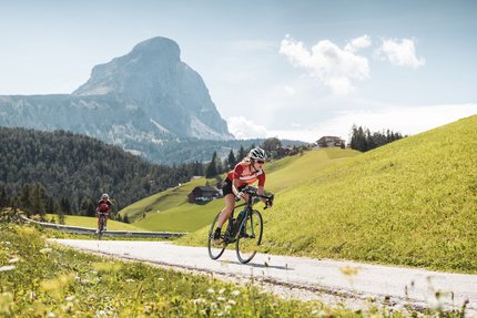 Zwei Radfahrer fahren auf Bergstraße mit Gipfel in der Sonne
