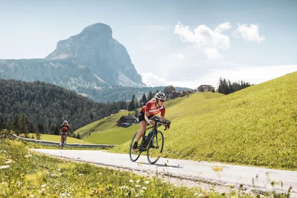 Zwei Radfahrer fahren auf Bergstraße mit Gipfel in der Sonne