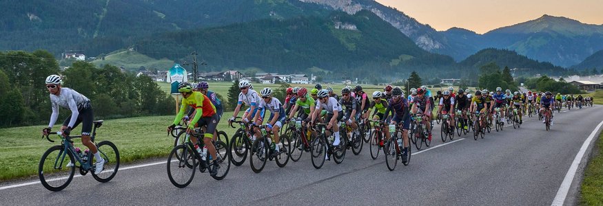 Viele Radfahrer fahren auf einer Landstraße mit Bergen im Hintergrund