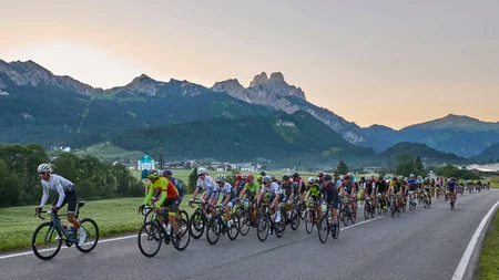 Grande gruppo di ciclisti su strada di campagna con montagne sullo sfondo