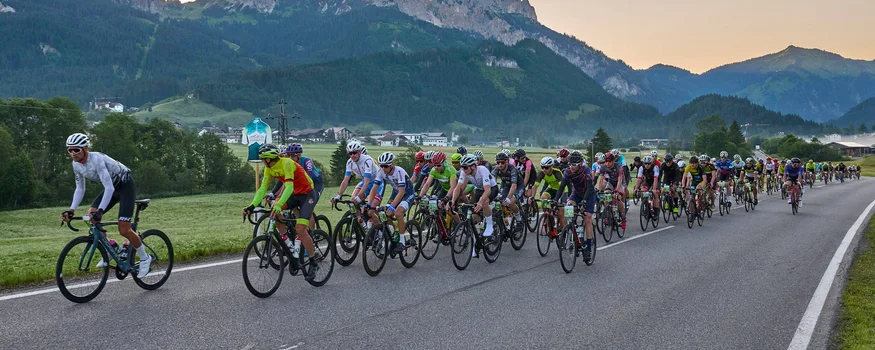 Viele Radfahrer fahren auf einer Landstraße mit Bergen im Hintergrund