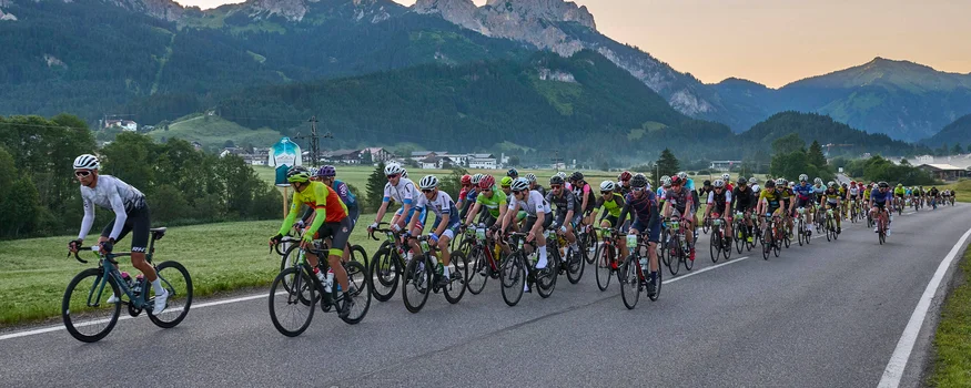 Grande gruppo di ciclisti su strada di campagna con montagne sullo sfondo