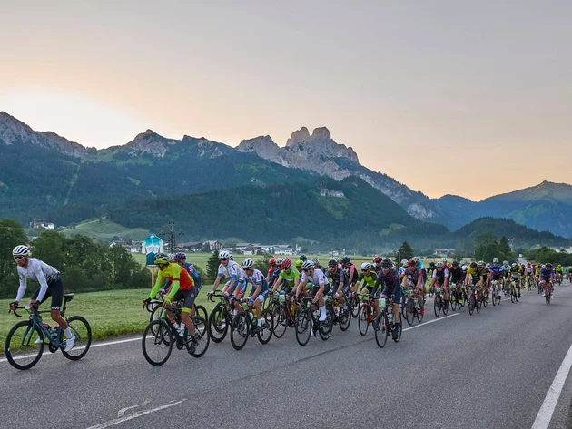 Grande gruppo di ciclisti su strada di campagna con montagne sullo sfondo