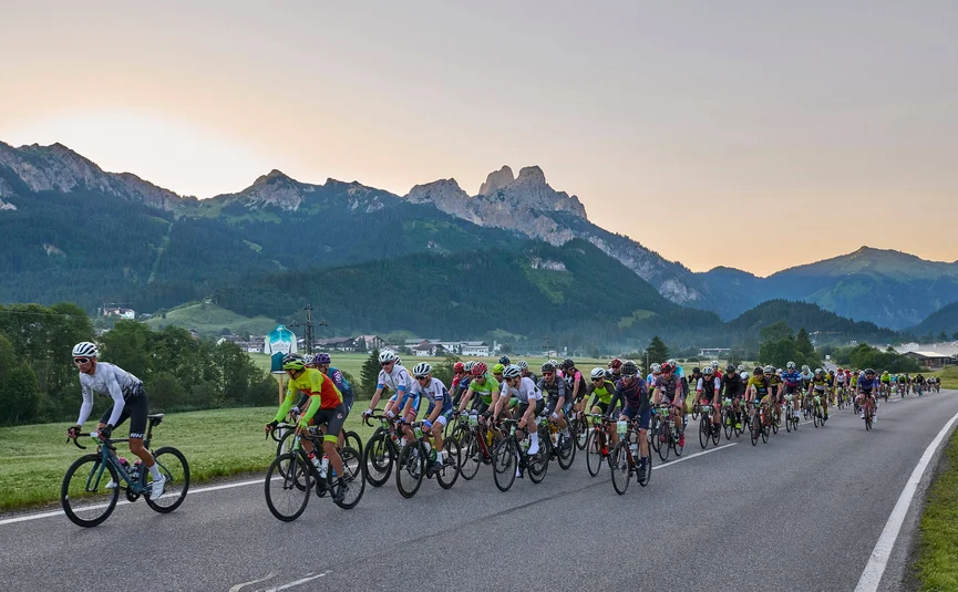 Viele Radfahrer fahren auf einer Landstraße mit Bergen im Hintergrund