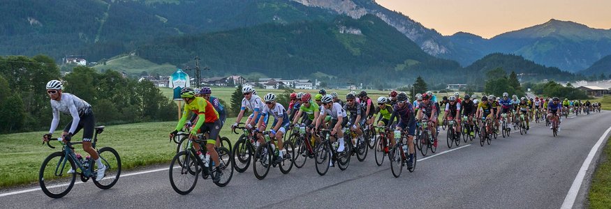 Grande gruppo di ciclisti su strada di campagna con montagne sullo sfondo