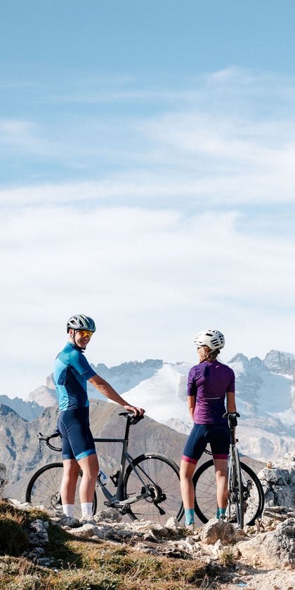 Two cyclists standing with their bikes on a mountain trail in clear weather