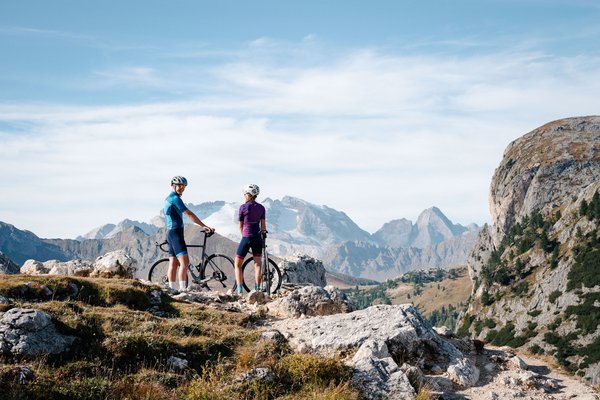Two cyclists standing with their bikes on a mountain trail in clear weather