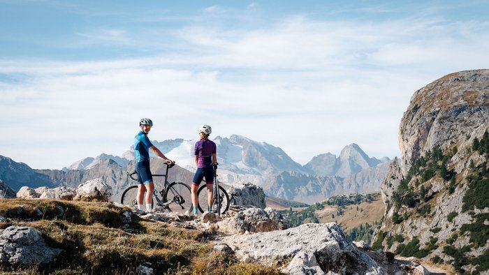 Two cyclists standing with their bikes on a mountain trail in clear weather