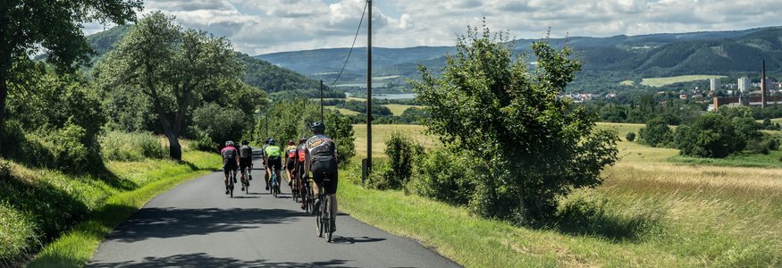 Gruppo di ciclisti su strada di campagna con paesaggio e tempo soleggiato