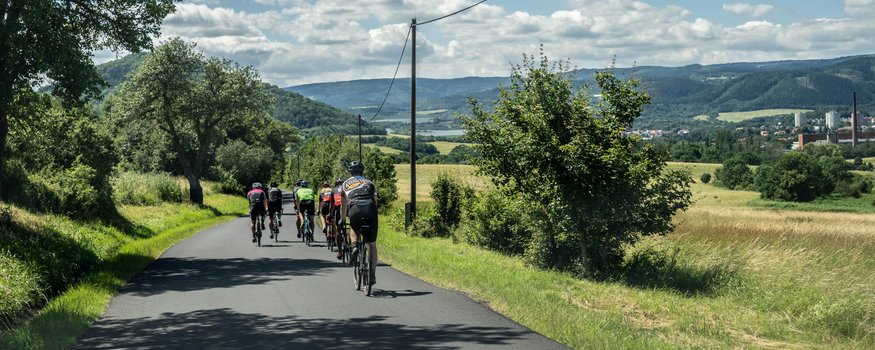 Gruppo di ciclisti su strada di campagna con paesaggio e tempo soleggiato