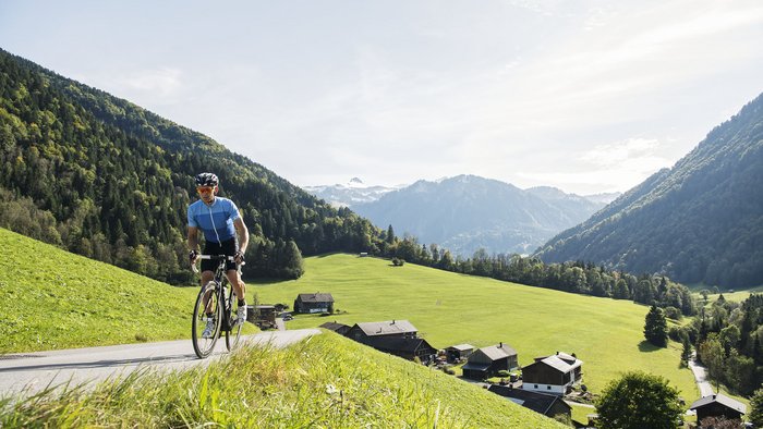 Man cycling on rural road in mountainous area with houses and green fields