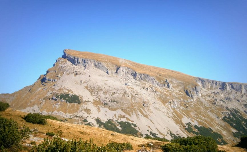 Berg met rotsachtige top en kale hellingen onder een heldere blauwe lucht