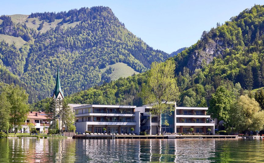 Modern buildings by lake with forested mountains and church steeple