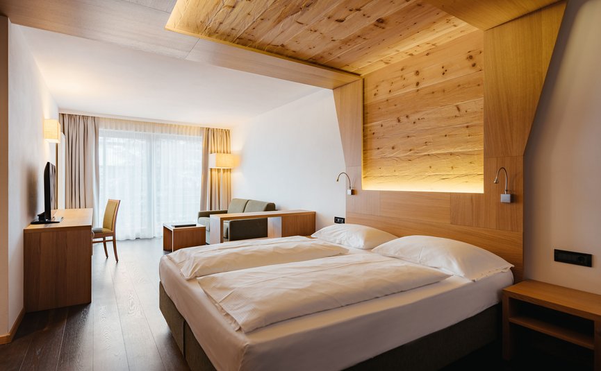 Camera d'hotel moderna con arredi in legno, letto matrimoniale e area salotto