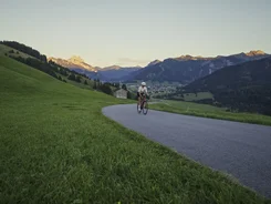 Fietser op bergweg met groen veld en bergzicht bij zonsondergang