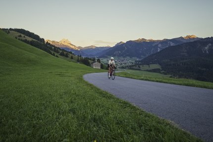 Cyclist on mountain road with green fields and mountain view at sunset