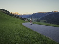 Tannheimer Valley © Wolfgang Ehn Cyclist on mountain road with green fields and mountain view at sunset