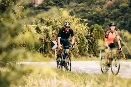 Twee wielrenners op weg met kasteel in bosrijk landschap