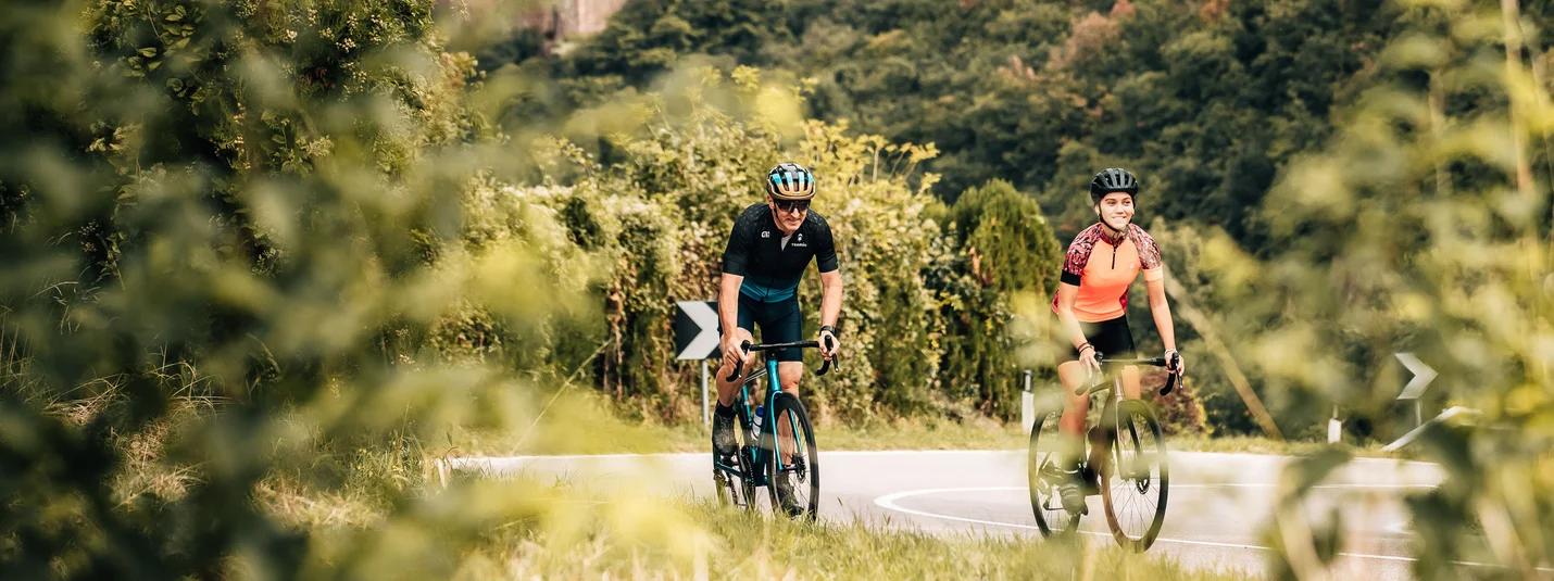 Adige Valley Tour © Jens Scheibe Two cyclists on road with castle in forested landscape background