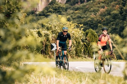 Two cyclists on road with castle in forested landscape background