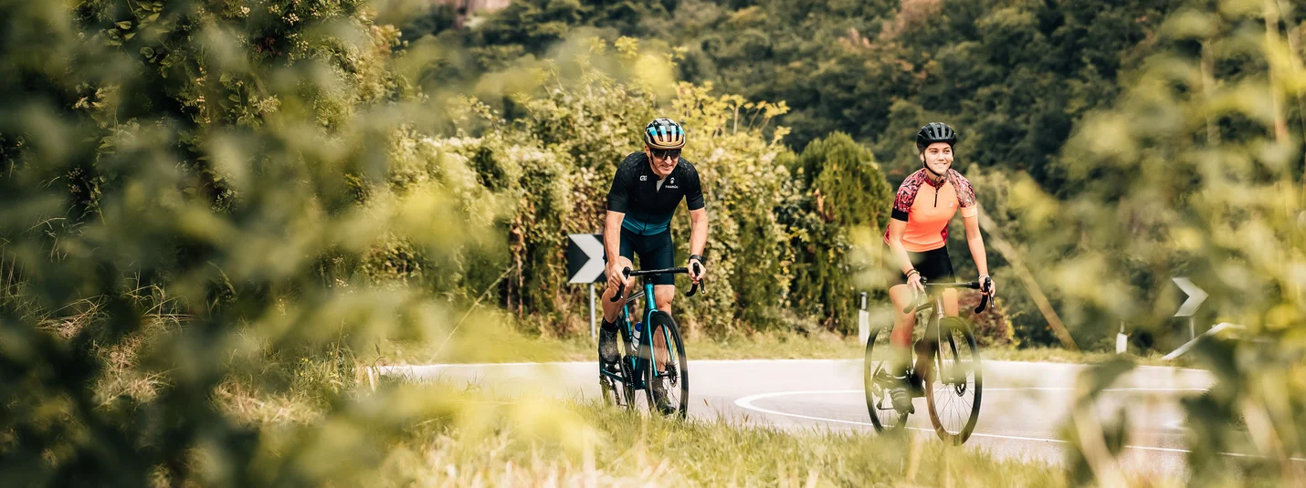 Tour della Valle dell'Adige © Jens Scheibe Due ciclisti su strada davanti a un castello in paesaggio boschivo