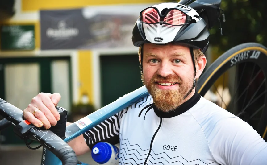 Ciclista con casco che porta la bici sulla spalla sorride alla fotocamera