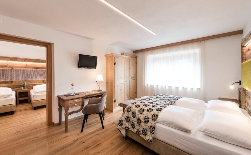 Bright hotel rooms with double and single beds, wooden furniture, and modern decor