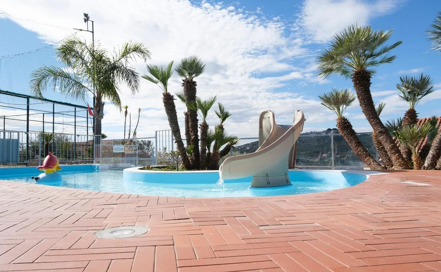 Small pool with slide and palm trees on terrace under sunny sky