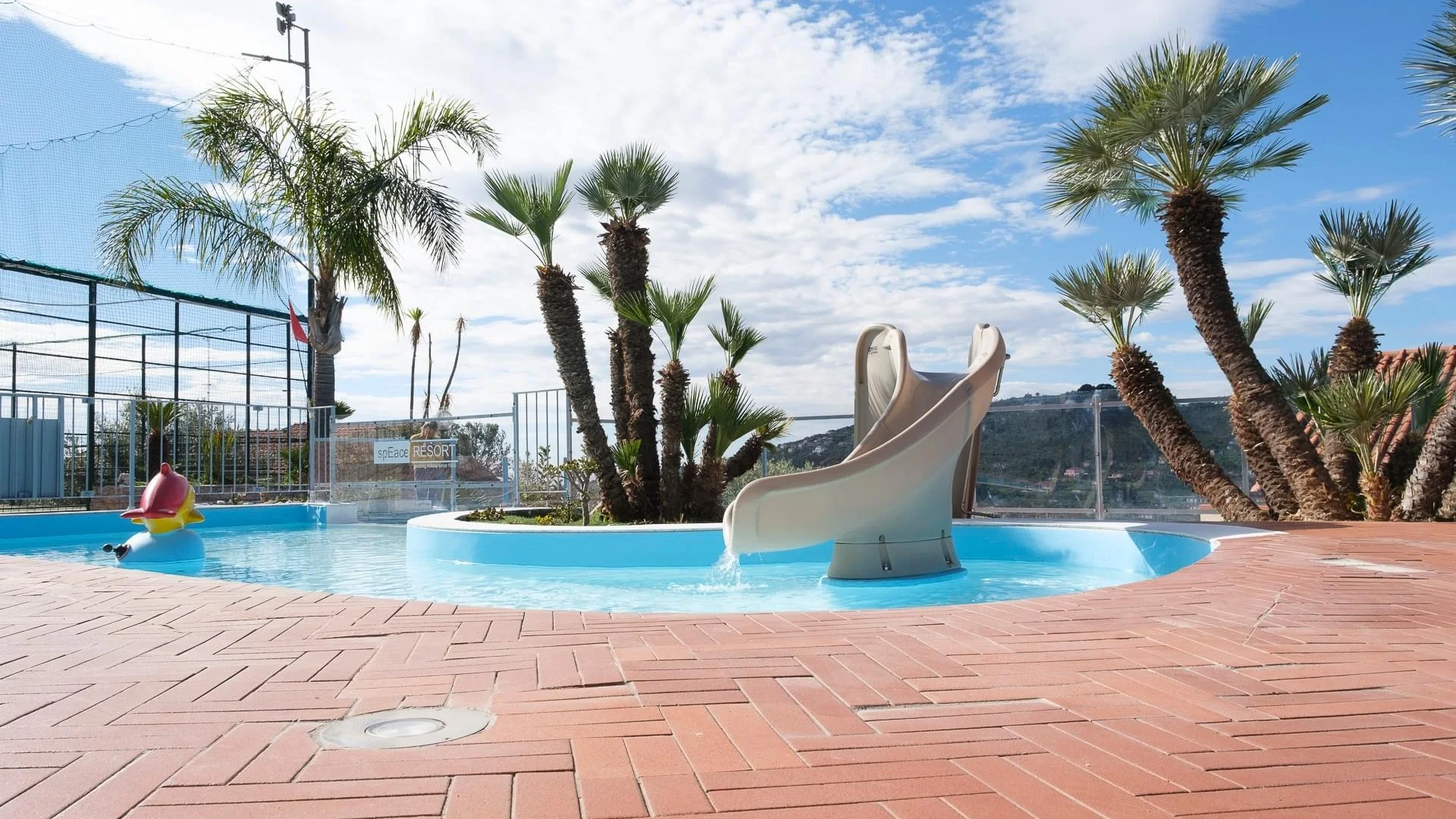 Kleiner Pool mit Rutsche und Palmen auf einer Terrasse bei sonnigem Himmel