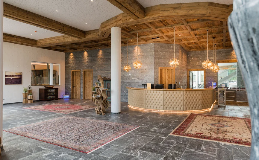 Hotelreceptie met rustiek houten plafond en decoratieve tapijten op stenen vloer