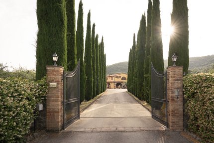 Ingangspoort naar landgoed met cipressen en huis op de achtergrond