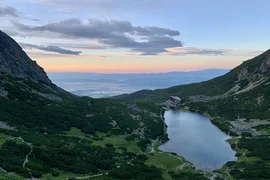 Bergsee und Hütte umgeben von grünen Hügeln bei Sonnenuntergang