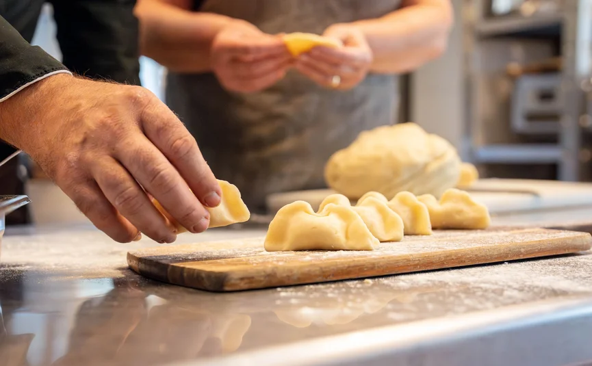 Mani che formano ravioli freschi su un tagliere in cucina