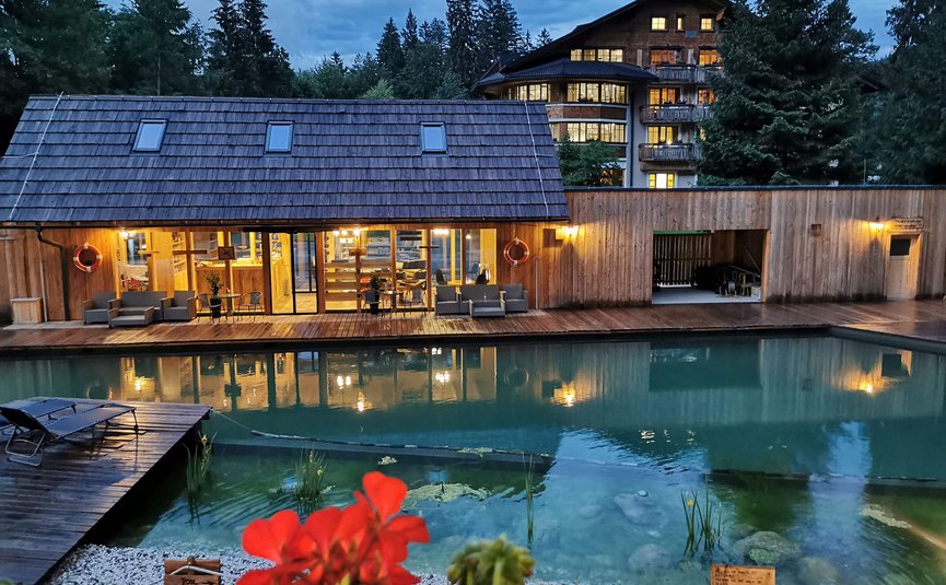 Area piscina in legno illuminata con sedute e edificio nel bosco al tramonto