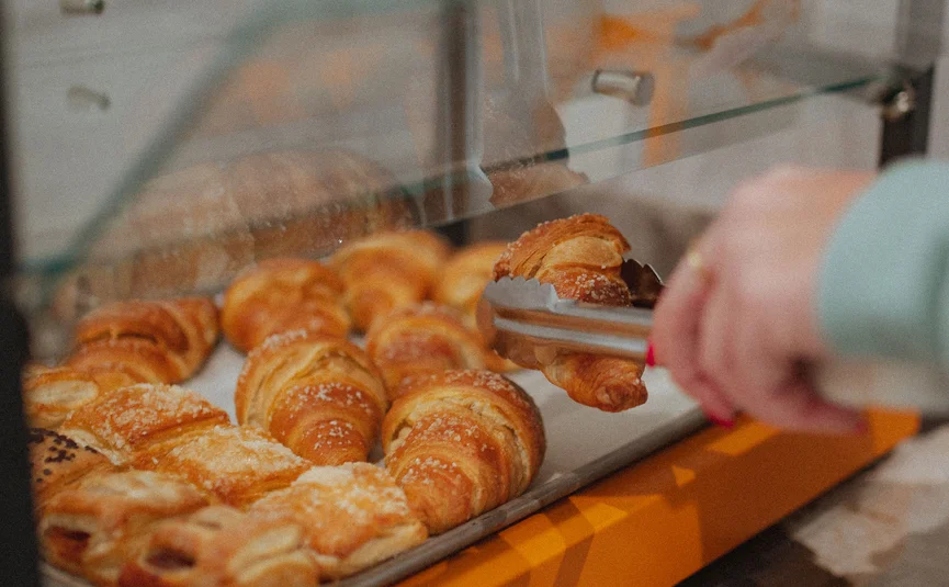Hotel Capris **** © Hotel Capris Capodistria Boutique Persoon pakt verse croissant uit bakkerijvitrine met een tang