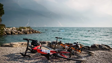 Zwischen Passstraßen, See & Dolce Vita beim Rennradurlaub am nördlichen Gardasee © Alex Moling Zwei Rennräder liegen am Ufer eines Sees mit Bergen im Hintergrund