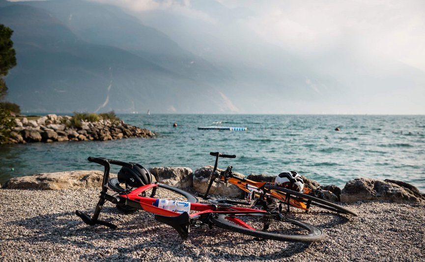 Due biciclette da corsa sdraiate sulla riva di un lago con montagne sullo sfondo