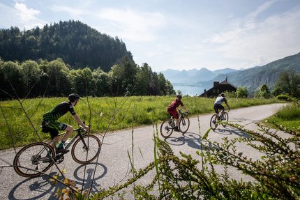 Tre ciclisti su una strada di campagna in un paesaggio montano soleggiato