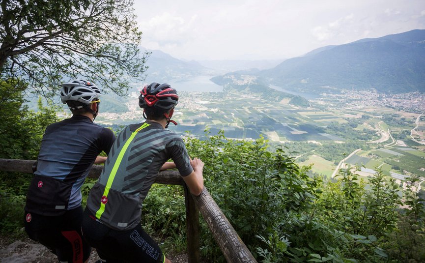 Due ciclisti osservano una valle e montagne da un punto panoramico verde.