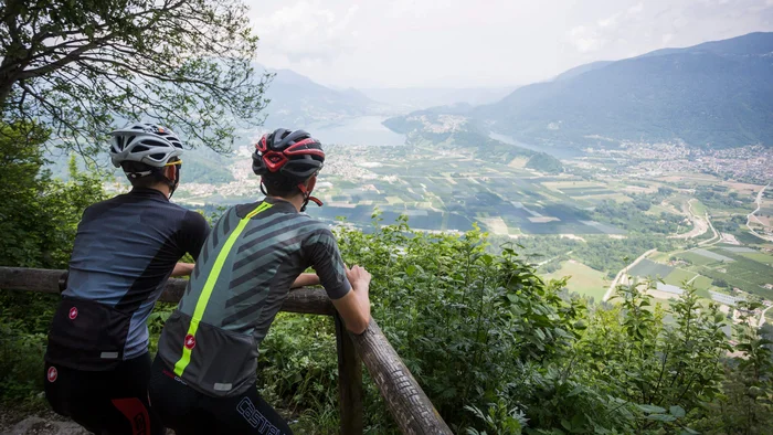 Zwei Radfahrer genießen Aussicht auf Tal und Berge von einem bewachsenen Aussichtspunkt.