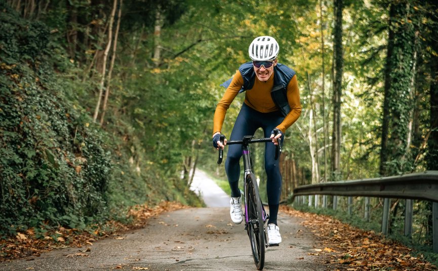 Uomo in bici da corsa in salita su sentiero nel bosco in autunno