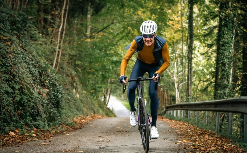 Mann fährt Rennrad bergauf auf Waldweg im Herbst